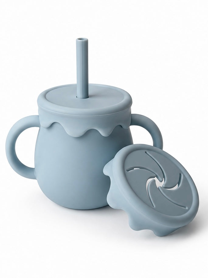 A light blue-gray silicone baby tumbler with side handles, a matching lid and straw, and a separate swivel lid placed in front, shown on a clean white background.
