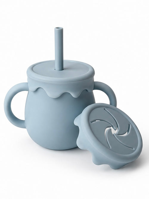 A light blue-gray silicone baby tumbler with side handles, a matching lid and straw, and a separate swivel lid placed in front, shown on a clean white background.