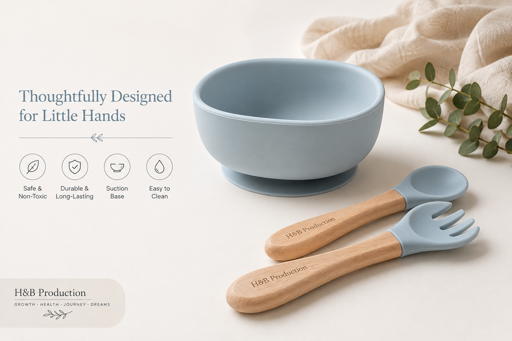 A light blue silicone baby bowl with a suction base, shown with a matching blue spoon and fork that have natural wood handles. The set is styled on a cream background with a beige cloth and green leaves, featuring marketing text on the left.